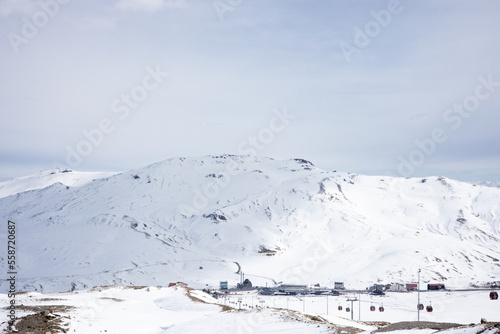 Snow-capped mountain ski slopes with ski lifts against cloudy sky and village in the valley. Winter vacation. Extreme sport and travel content. © DiandraNina