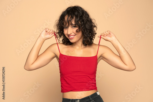 Photos Young exotic happy brunette woman in red sleeveless shirt and jeans posing  on a