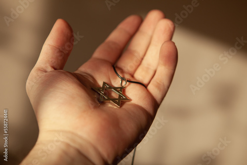 Closeup of pendant in the shape of the star of david on the hand of a man. Holocaust remembrance day.
