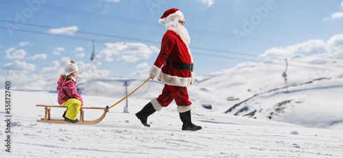 Santa claus pulling a girl on a wooden sleigh at a snowy mountain