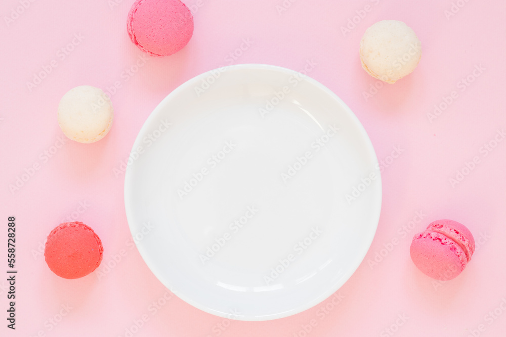 Empty white plate on pink background, macaroon cookies around it. Girly, romantic colors, vertical view Empty white plate on pink background, macaroon cookies around it. Girly, romantic colors, vertical view