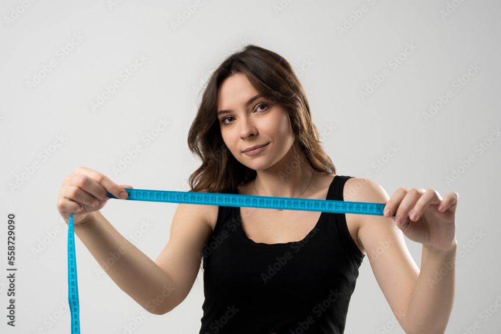 Slim young beautiful brunette girl in black underwear with a measuring tape in front of her face. Photo of beautiful brunette girl with perfect body. Fitness or body care concept. Slim young beautiful brunette girl in black underwear with a measuring tape in front of her face. Photo of beautiful brunette girl with perfect body. Fitness or body care concept.