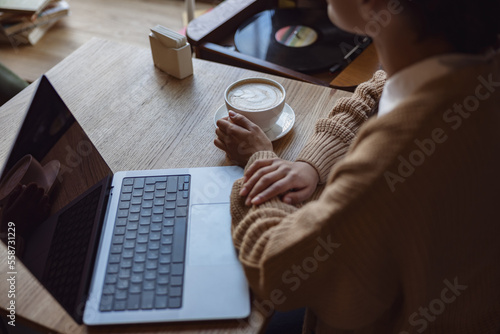 Overhead view of a woman drinking coffee and using laptop with empty blank screen at a cafe. Copy space