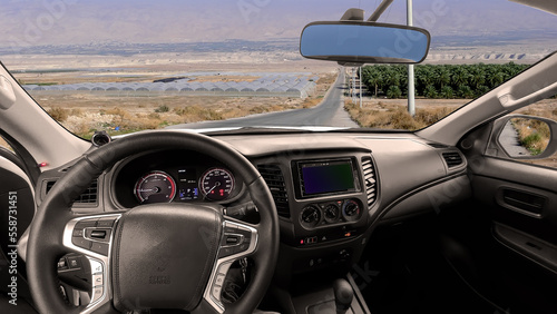 Steering wheel and dashboard of the car with view through the windshield on a panoramic view of the agricultural Jordan Valley