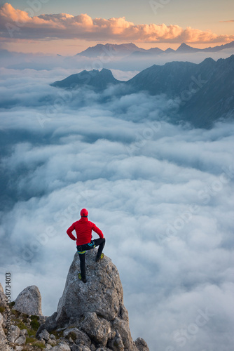 Mountaineer on the top of the mountain admires the landscape during sunrise, Pizzo Badile Camuno, Valle Camonica, Lombardy, Italy.