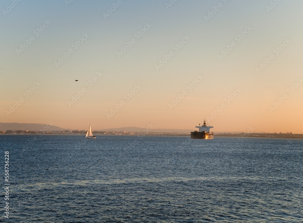 Ship and sailboat on the Tagus River at sunset in Lisbon, Portugal