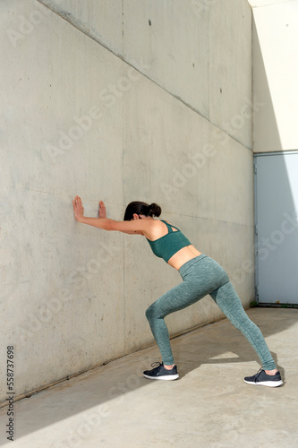 woman doing a calf or leg stretch against a concrete wall outside, warm up exercises.