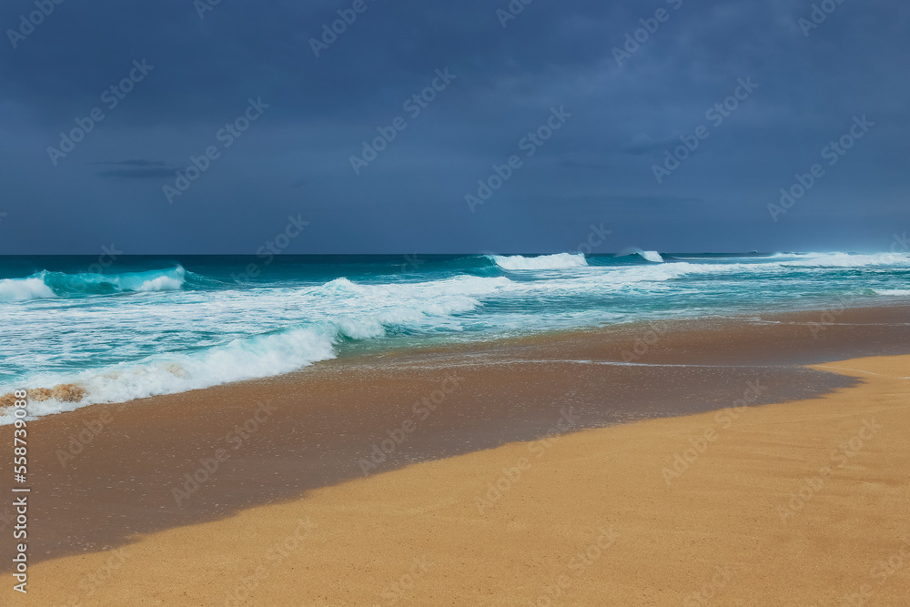 Tropical beach on an overcast day with turquoise waves crashing onto sandy shore