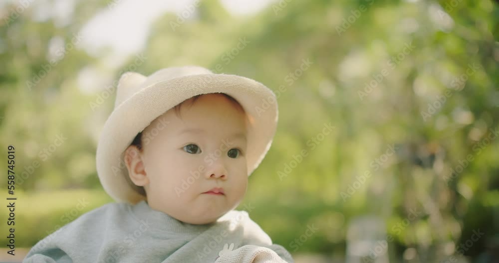 Portrait little cute adorable Asian baby toddler girl in hat having good time sitting at the park eating cookie and looking at green nature plant tree outdoor in vacation holiday summertime Portrait little cute adorable Asian baby toddler girl in hat having good time sitting at the park eating cookie and looking at green nature plant tree outdoor in vacation holiday summertime