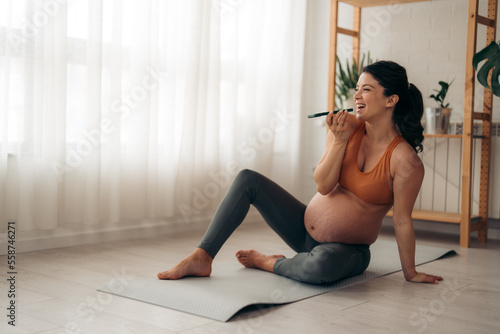 Pregnant woman talking on the smart phone and resting on a mat after workout at home.