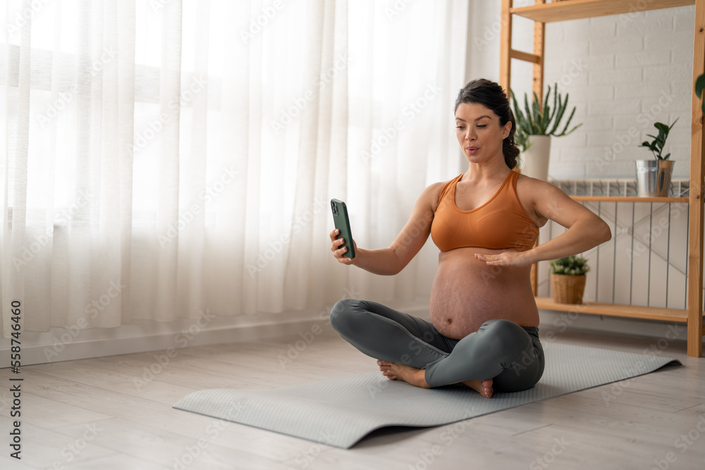 Pregnant woman using online app to practice breathing exercise while sitting on a mat at home.