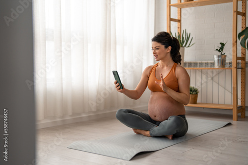 Pregnant woman using phone while doing yoga at home