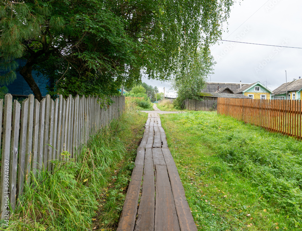 Rustic wooden walkways along a wooden fence among green grass.