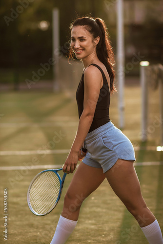 Girl with dark hair on the tennis court with a tennis racket posing in a black bodysuit © Kaminski Vadim
