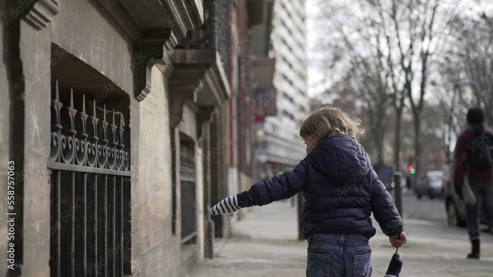 Little boy walking in urban street alone during winter. Toddler walks in sidewalk