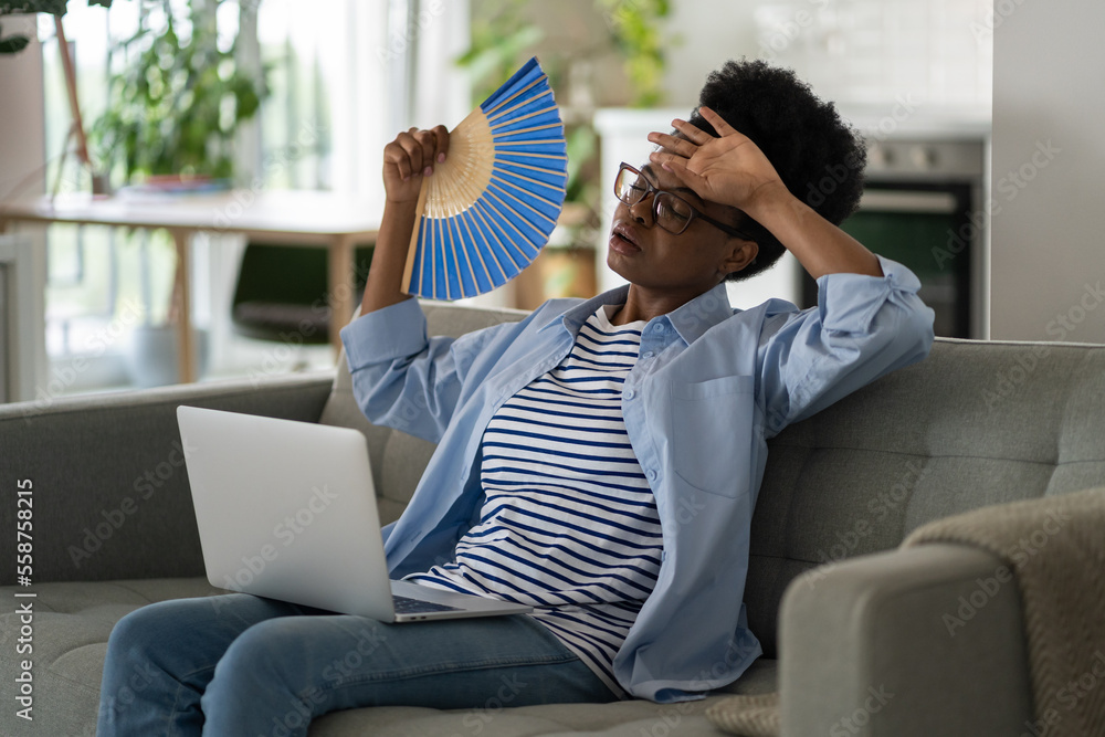 Tired depressed African American millennial woman using hand fan ...