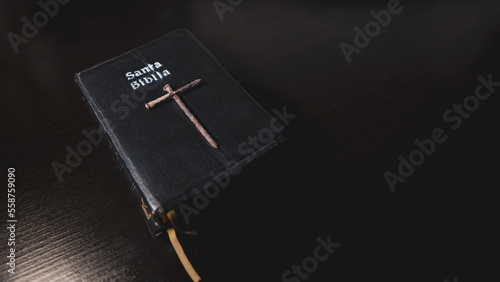Portada de santa biblia en una meza y clavos oxidados formando una cruz encima del escritorio de pintura negra y destellos de luz.