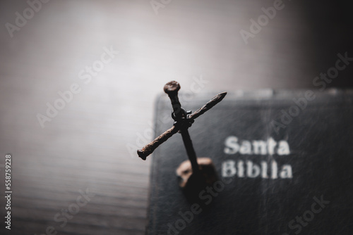 Portada de santa biblia en una meza y clavos oxidados formando una cruz encima del escritorio de pintura negra y destellos de luz. photo