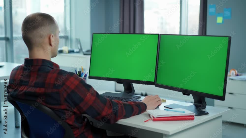 Young Man Working On Computer With Two Green Screen Mock Ups Sitting At Desk In Office Young Man Working On Computer With Two Green Screen Mock Ups Sitting At Desk In Office