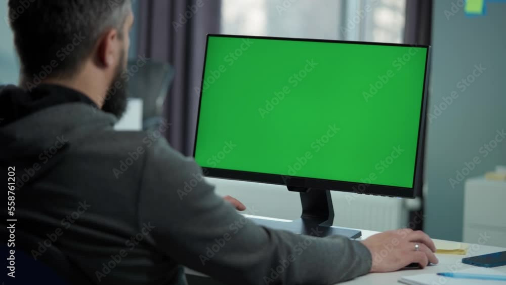 Man Working At Computer With Green Mock Up Screen Sitting At Desk in Office. Desktop Computer Monitor with Mock Up Green Screen Chroma Key Display Standing on Desk Man Working At Computer With Green Mock Up Screen Sitting At Desk in Office. Desktop Computer Monitor with Mock Up Green Screen Chroma Key Display Standing on Desk