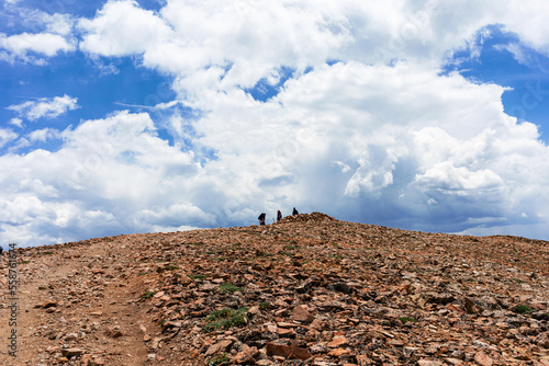 Hikers at the crest of Mount Bross at 14, 172 with rocky path leading to the crest with blue sky and cumulus clouds