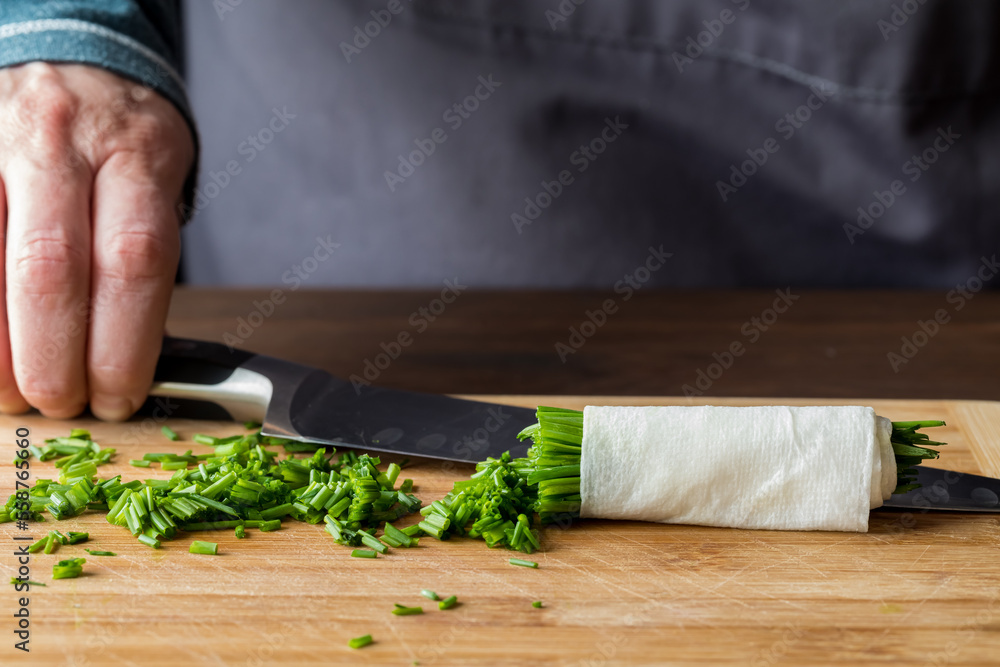 A chef holding a sharp knife in behind a freshly chopped pile of chives. A chef holding a sharp knife in behind a freshly chopped pile of chives.