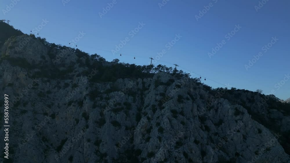 The camera flies from below to the top of the mountain, along which the funicular rides against the blue sky. High quality 4k footage The camera flies from below to the top of the mountain, along which the funicular rides against the blue sky. High quality 4k footage