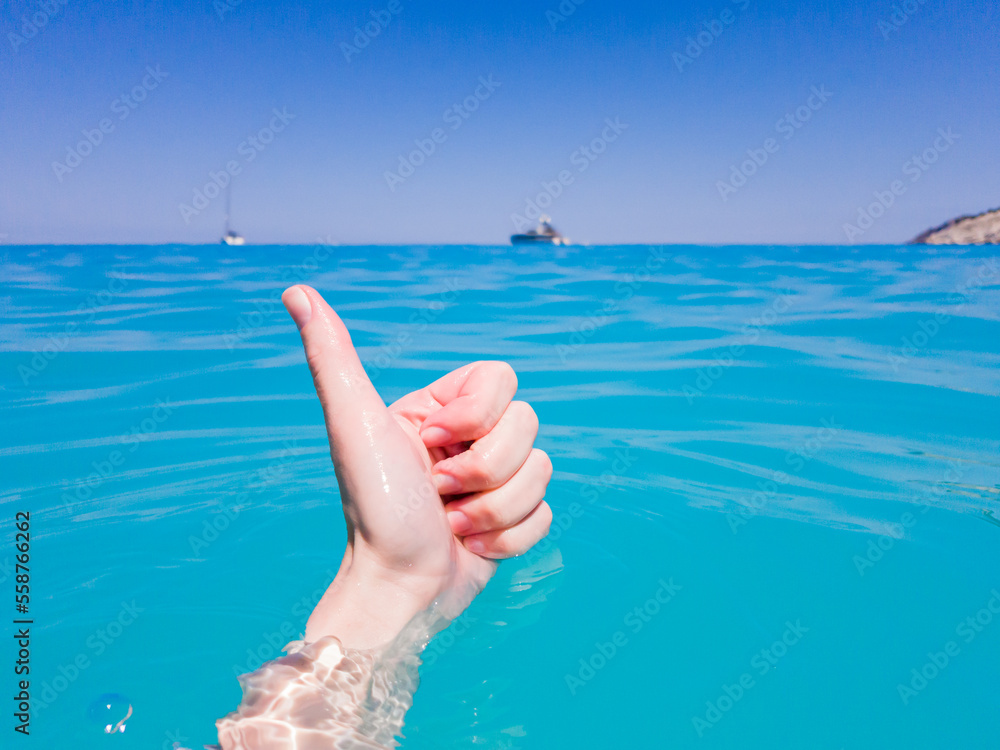 Thumbs up sign from pure and transparent sea water at Myrtos Beach. Summer scenery of famous and extremely popular travel destination in Cephalonia, Greece, Europe Thumbs up sign from pure and transparent sea water at Myrtos Beach. Summer scenery of famous and extremely popular travel destination in Cephalonia, Greece, Europe
