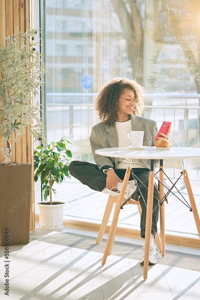 Young smiling african american girl drinking coffee and eating tasty croissant in a cozy cafe. Holidays, lunch time and vacation concept Young smiling african american girl drinking coffee and eating tasty croissant in a cozy cafe. Holidays, lunch time and vacation concept