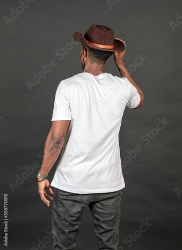 Back side image of an african man wearing white blank shirt with a hat, doing a simple pose by putting one of his hand on his hat