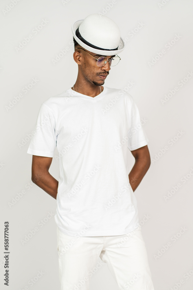 An african man wearing white blank shirt with a hat and glasses, doing a pose with both of his hand on his back, on the white background