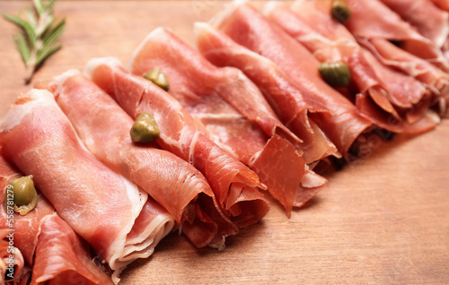 Slices of delicious ham and capers on wooden background, closeup