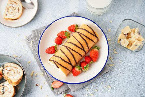 Plate with delicious sponge cake roll, fresh strawberries and glass of milk on light background