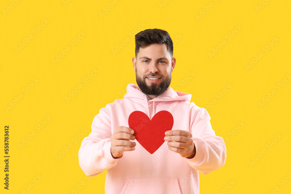 Young bearded man with paper heart for Valentine's Day on yellow background Young bearded man with paper heart for Valentine's Day on yellow background