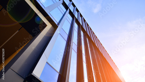 Glass modern building with blue sky background. Low angle view and architecture details. Urban abstract - windows of glass office building in  sunlight day.