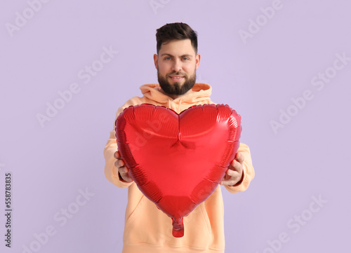 Young bearded man with balloon for Valentine's Day on lilac background © Pixel-Shot