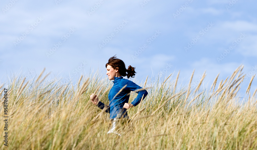 A woman running along a sandy trail with tall grass at the ocean. A woman running along a sandy trail with tall grass at the ocean.