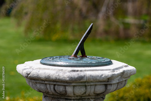 A brass sundial or shadow clock on a decorative concrete pedestal with a single metal angle rod celestial instrument. The sun dial measures the time on the mathematical clock using sunlight and shadow