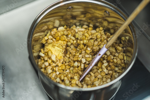 Cubed apple and butter seasoned with cinnamon in metal pot. Spatula being put in the pot. High quality photo