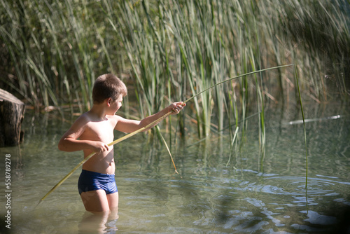 Fototapeta Naklejka Na Ścianę i Meble -  Lonely boy admiring the beauty of the summer lake in greece . Boy playing outside - imitate fishing at a lake.