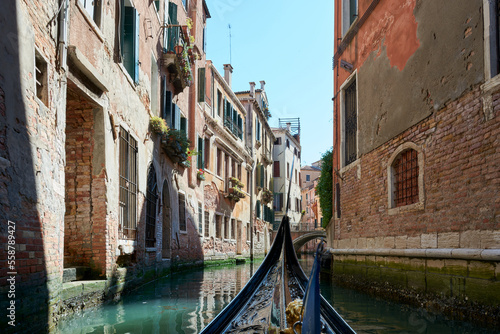 View from gondola with narrow canal of water surrounded by old buildings on sunny day in Venice, Italy. © Eduardo Accorinti