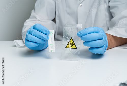 Toronto, Ontario, Canada - December 30, 2022: Hand displaying placement of rapid test cassette with specimen in biohazard waste plastic bag. Covid-19 antigen rapid test kit. photo