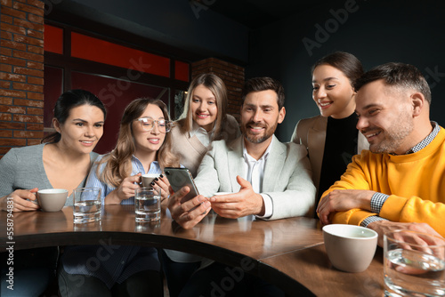 Handsome man showing something funny in smartphone to his friends in cafe