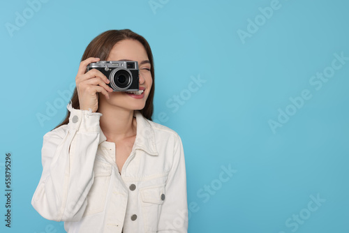Young woman with camera taking photo on light blue background, space for text. Interesting hobby