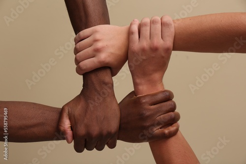 Men joining hands together on beige background, closeup