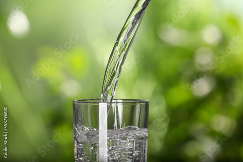 Pouring water into glass outdoors, closeup view