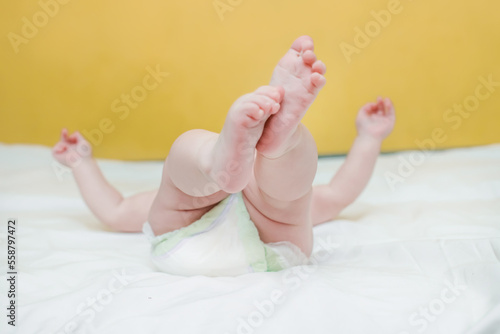 The pink heels of a small baby baby lying on his back on a white bed and playing with his own hands. Caring for the child. Change diapers for newborns.