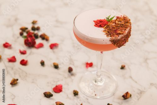 A sweet pink sparkling beverage decorated with crusted chocolate and small roses in a coupe glass.