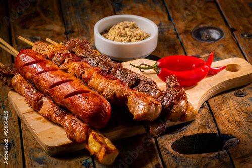 Espetinhos de churrasco em tábua de madeira com acompanhamentos, arroz, vinagrete, farofa e maionese photo