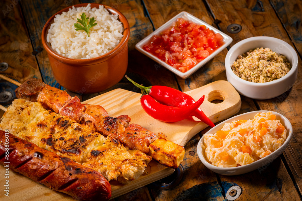 Espetinhos de churrasco em tábua de madeira com acompanhamentos, arroz, vinagrete, farofa e maionese Espetinhos de churrasco em tábua de madeira com acompanhamentos, arroz, vinagrete, farofa e maionese
